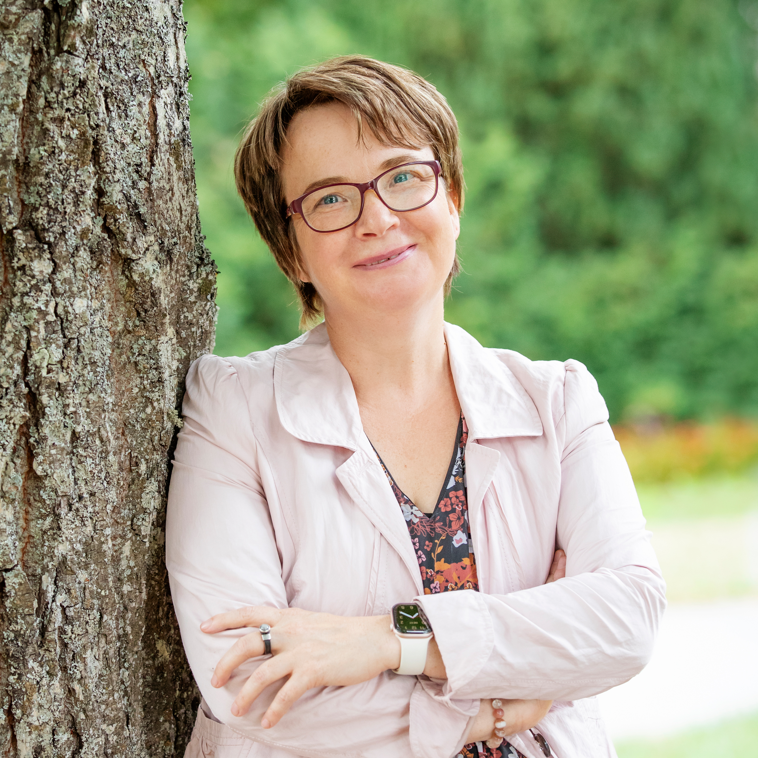 Trauerbegleiterin und Coach Michaela Fecht-Lehmann lächelt freundlich in die Kamera, angelehnt an einen Baum in grüner Natur.