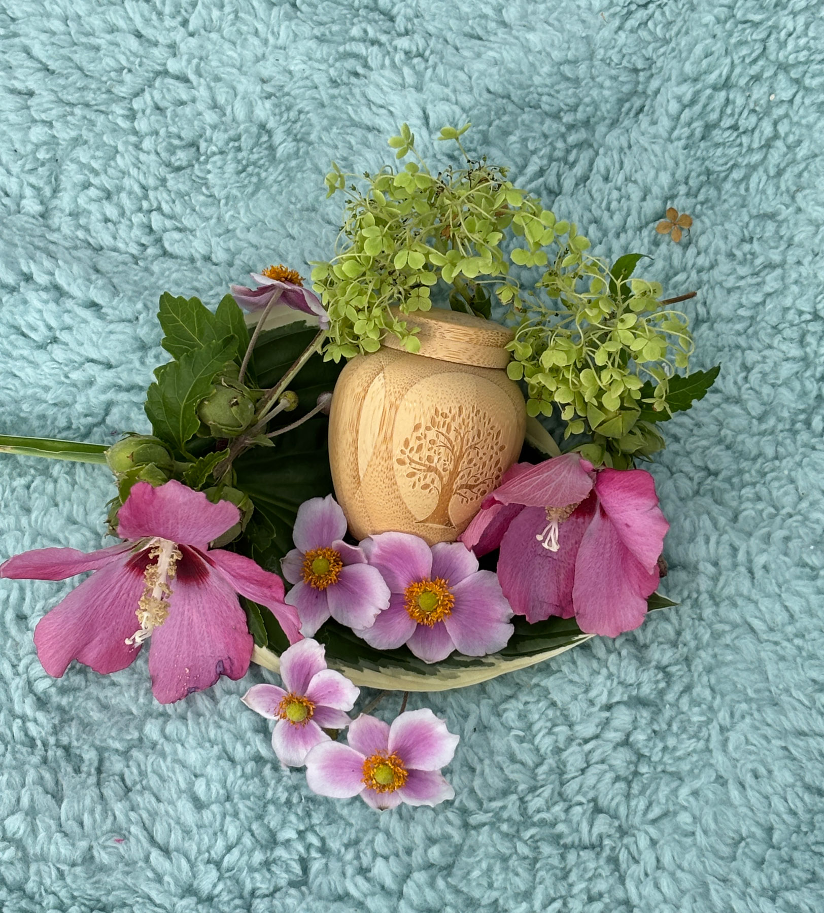 Kleine Tierurne aus Holz, umgeben von rosa Blüten und grünem Blattwerk, als Symbol für einen liebevollen Abschied vom Haustier.