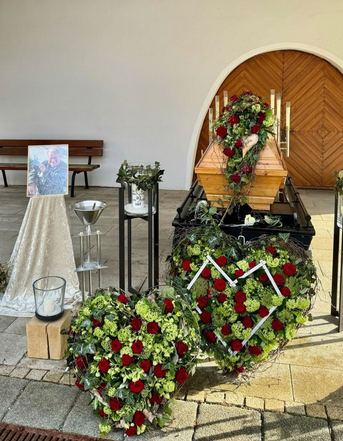 Ein mit Blumen geschmückter Sarg mit Kränzen und einem Gedenkfoto an den Verstorbenen